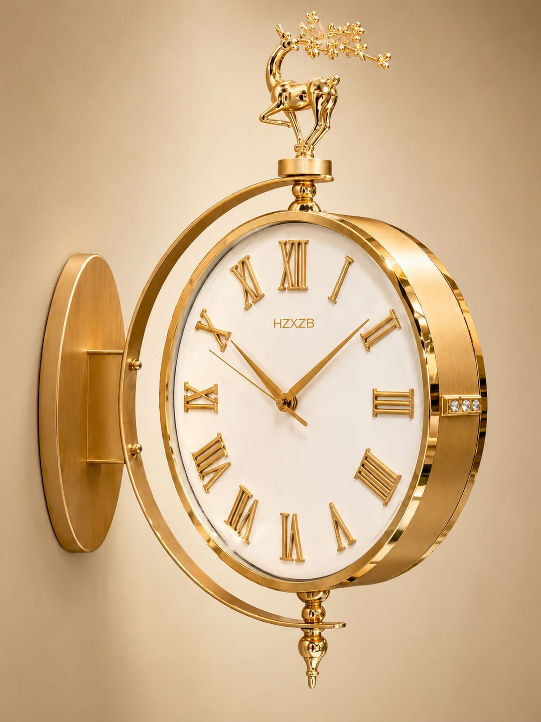 A luxury gold wall clock with a white dial, Roman numerals, and a decorative gold deer figurine on top, mounted on a beige wall.