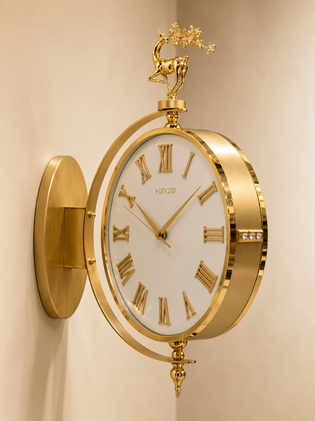 Gold wall clock with a white dial, Roman numerals, and a decorative deer and tree sculpture on top, mounted on a beige wall.