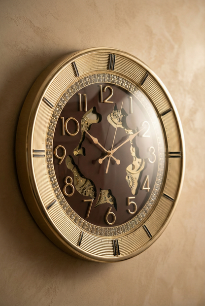 16-inch luxury designer wall clock with a gold metallic frame, brown dial, crystal-studded inner ring, raised gold numerals and exposed decorative gears mounted on a textured beige wall.