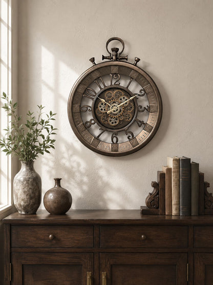A large round vintage-style wall clock with a skeletonized center and Roman numerals, mounted on a beige wall above a dark wood console table with vases and books.