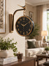 A round wall clock with a black face and gold trim, mounted on a gold-colored bracket shaped like a bird perched on a branch, shown in a styled living room setting.