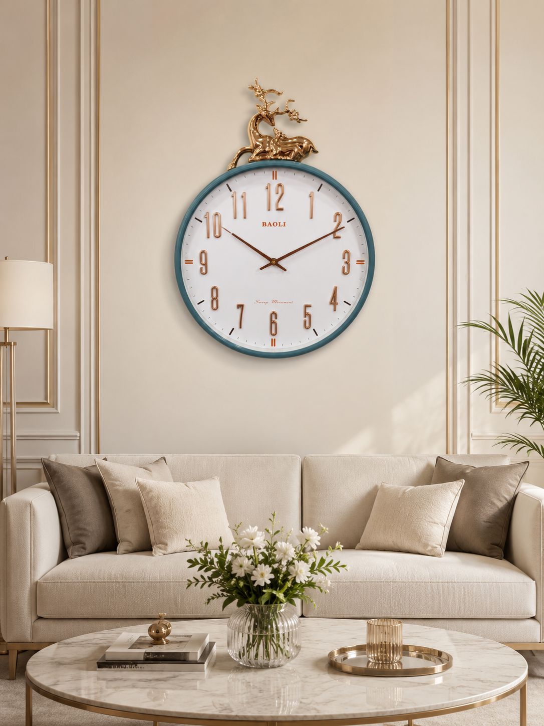A round wall clock with a white face, dark blue rim, and gold deer ornament hanging above a beige sofa in a styled living room.