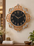 A wall clock with an ornate gold-tone frame, crystal-embellished details, and a black dial, mounted on a beige wall above a wooden console table with decorative items.