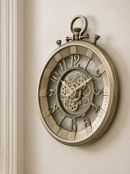 An antique-style round wall clock with a metallic bronze finish, featuring a skeletonized center showing intricate gears and cogs, set against a warm beige wall.