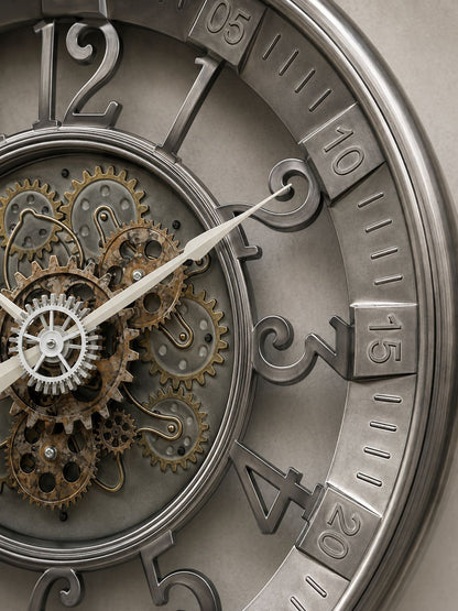 Close-up of a decorative wall clock face with exposed internal gears and cogs, large stylized numerals, and metallic silver and bronze tones.