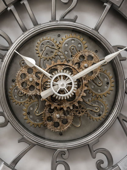 Close-up of a decorative wall clock face with exposed mechanical gears and cogs, silver-tone numerals, and white hands.