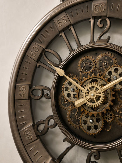 Close-up of a decorative wall clock with a bronze-toned metal frame, large Roman numerals, and a visible inner gear mechanism with brass-colored hands.