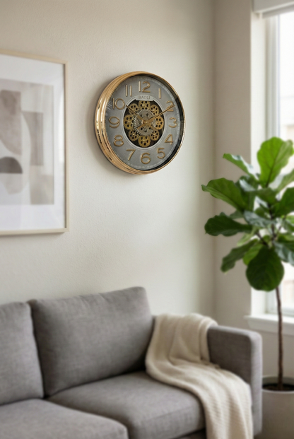 Decorative wall clock on a wall above a gray sofa with a plant in the corner.