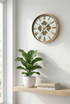 Decorative wall clock with a plant and books on a shelf in a bright room.