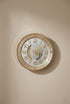 Decorative wall clock with gold and white design on a beige wall