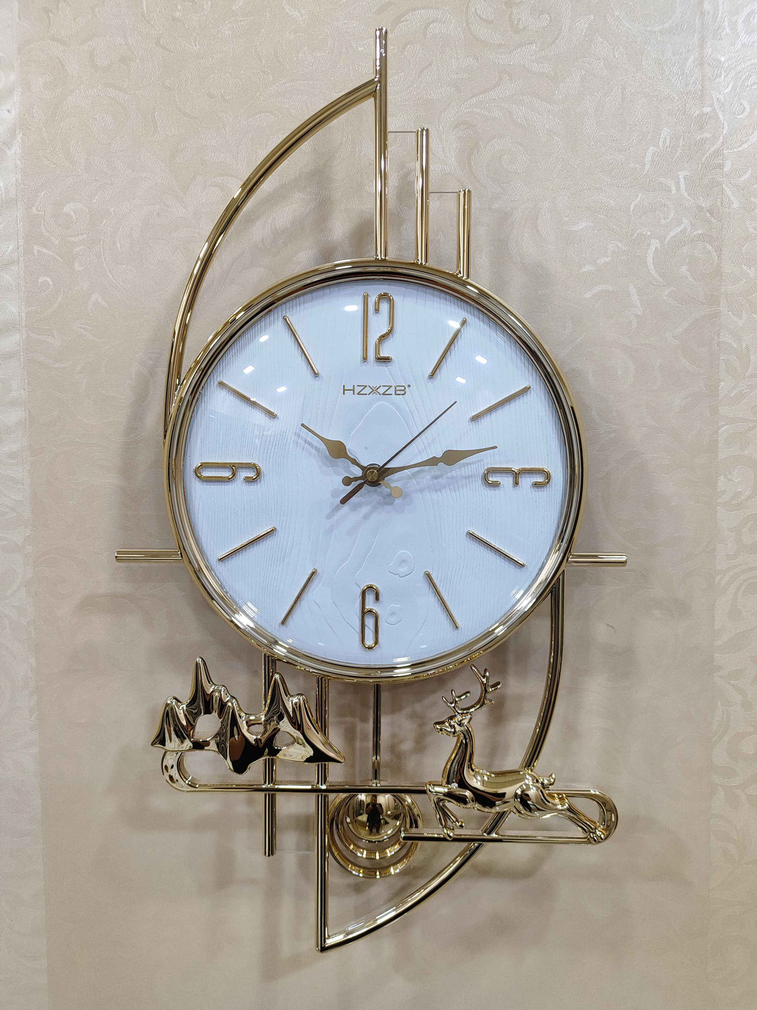 A decorative gold wall clock featuring a reindeer and mountain design, with a white clock face and gold hands.