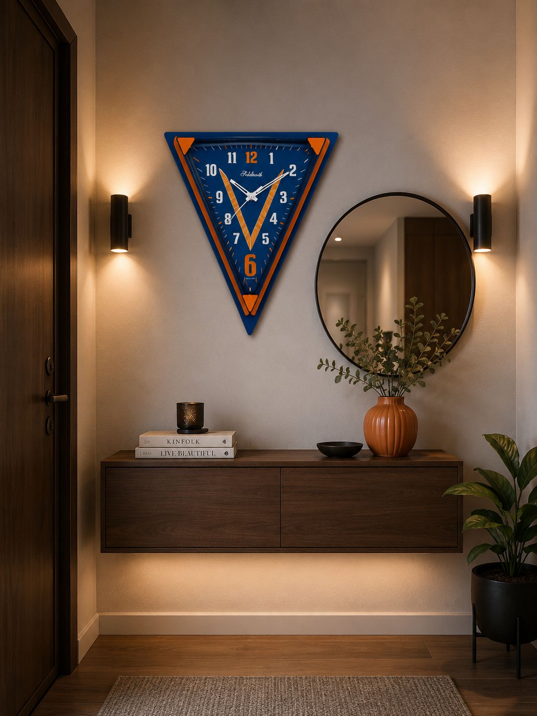A triangular wall clock with a blue and orange design hangs on a beige wall above a floating wooden console table in a modern hallway setting.