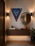 A triangular wall clock with a blue and orange design hangs on a beige wall above a floating wooden console table in a modern hallway setting.