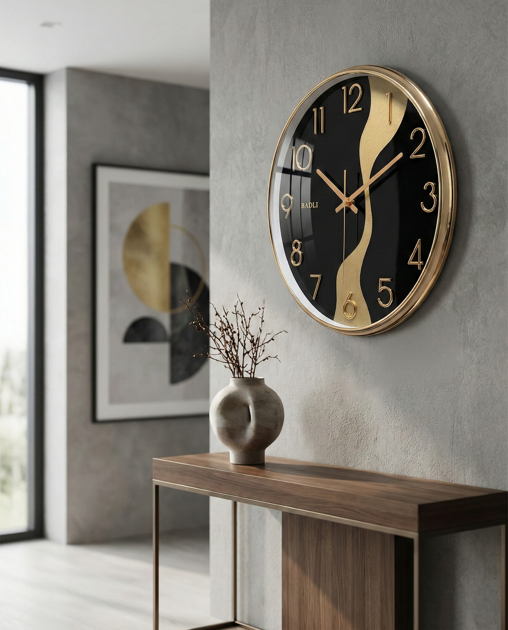 Modern wall clock with black and gold design on a gray wall, with a vase and abstract art in the background.