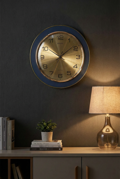 Wall clock on a dark wall with a lamp and books on a table below.