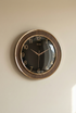 Wall clock with bronze frame and black face on a beige wall