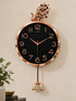 wall clock with a peacock top and hanging ornament, featuring a black dial and rose gold frame, shown mounted on a beige wall.
